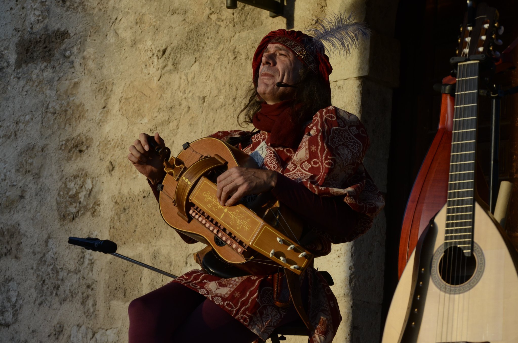 Hombre vestido con ropas tradicionales tocando un instrumento musical en una calle de piedra.