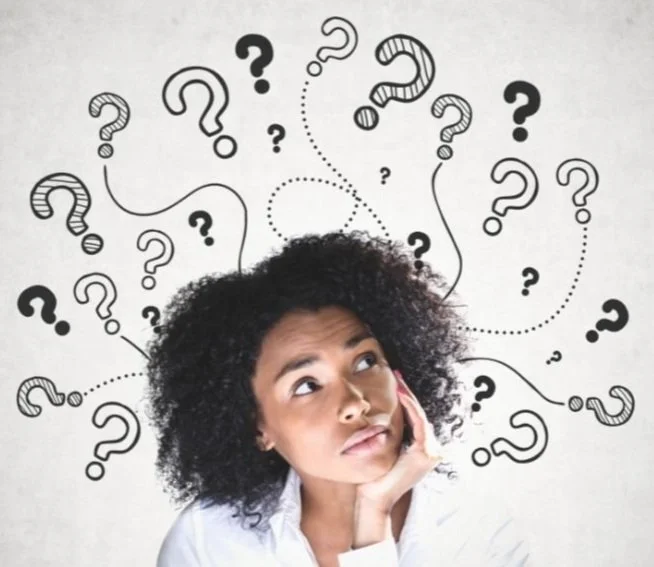 A woman of colour looking up to her left, thinking about something. Many question marks are all around her.
