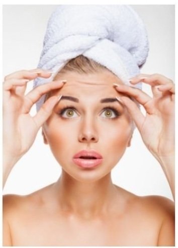 Woman with a white towel wrapped around her hair. She's touching the wrinkles on her forehead.