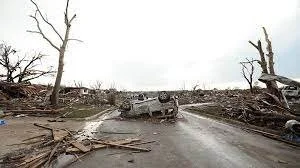 A damaged road with fallen trees and debris, showing destruction from a natural disaster or storm.