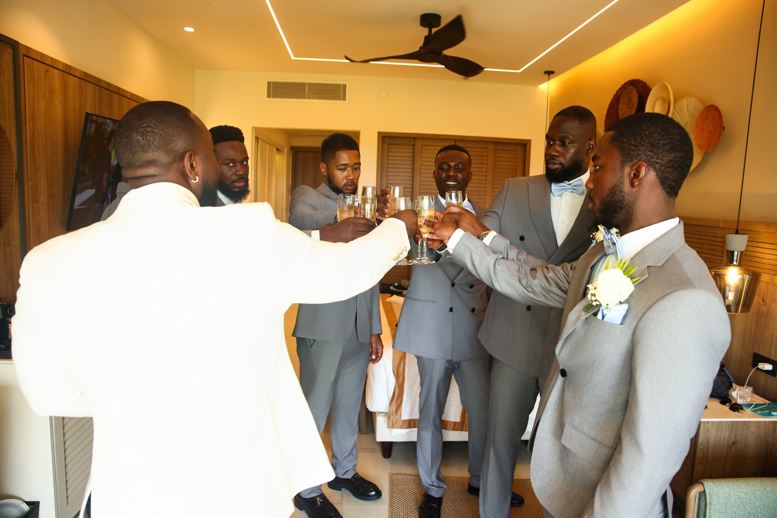 Group of men dressed in suits raising champagne glasses for a toast in a warmly lit room with decorative wall art.