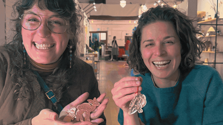 Two women smiling and holding small figurines in a store or market setting.