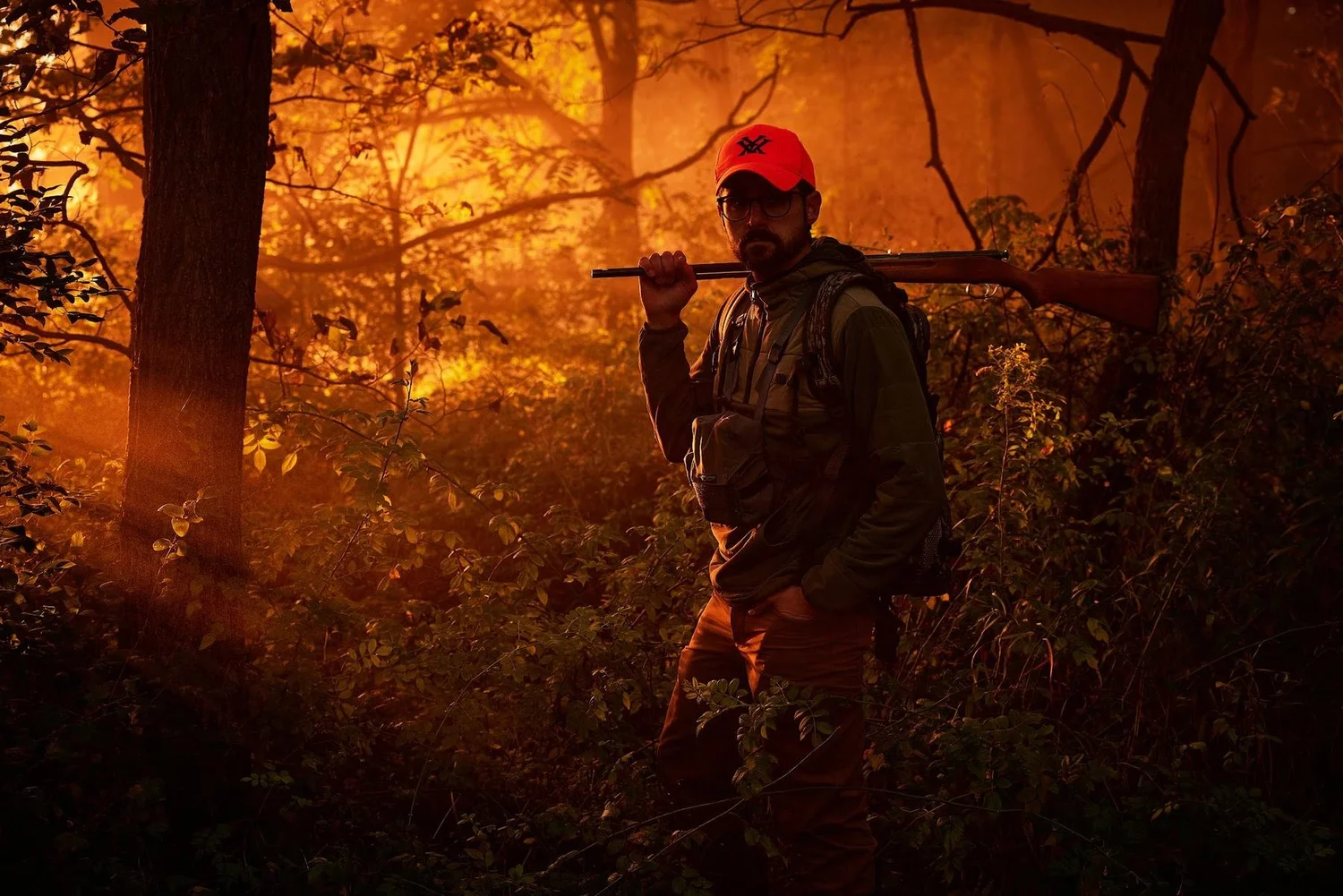 Hunter with a rifle over his shoulder in glowing orange forest light