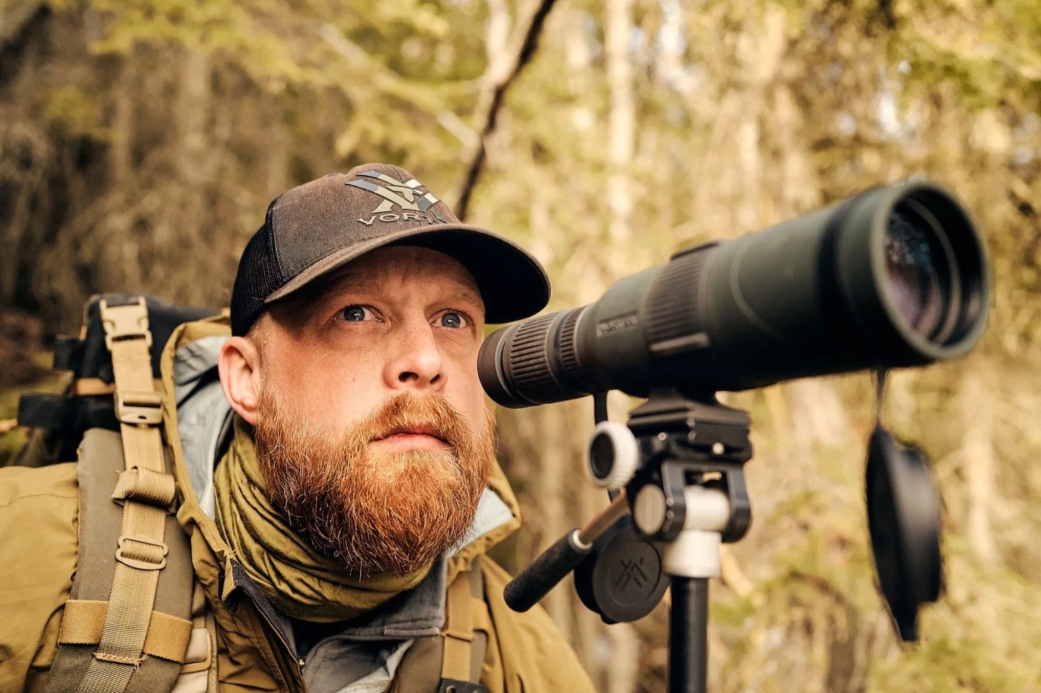 Bearded hunter behind a spotting scope on a tripod