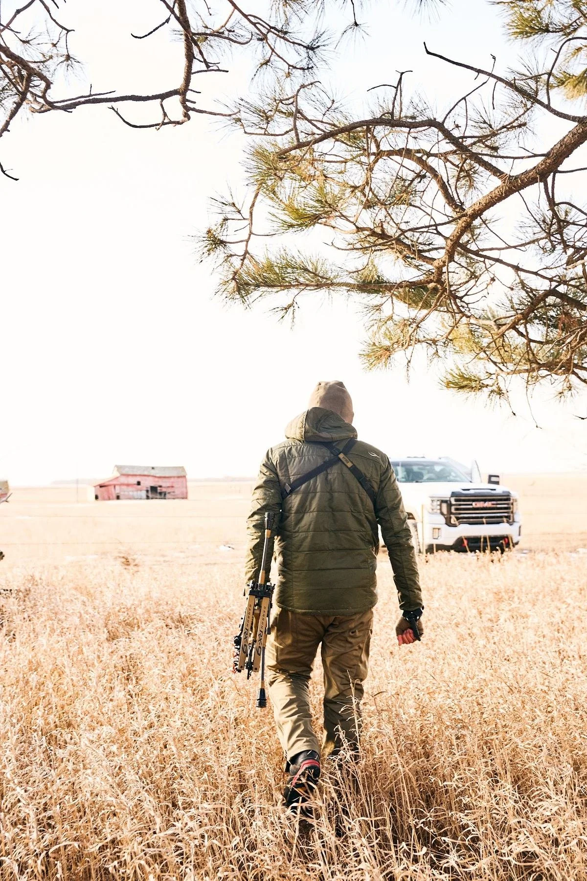 Bowhunter walking through tall prairie grass toward a white pickup and a red barn