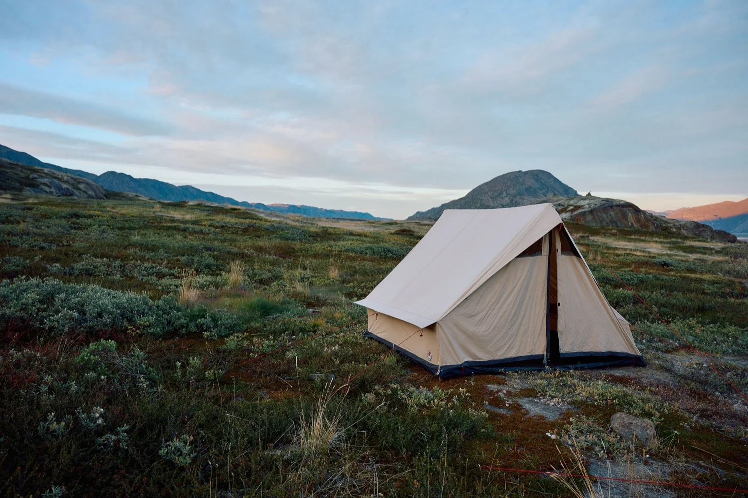Canvas wall tent on the tundra at sunset, fjord behind