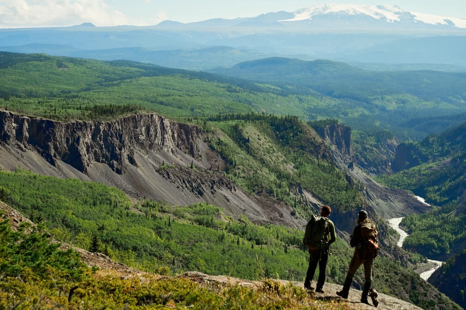 Two hunters on a canyon rim above a river valley