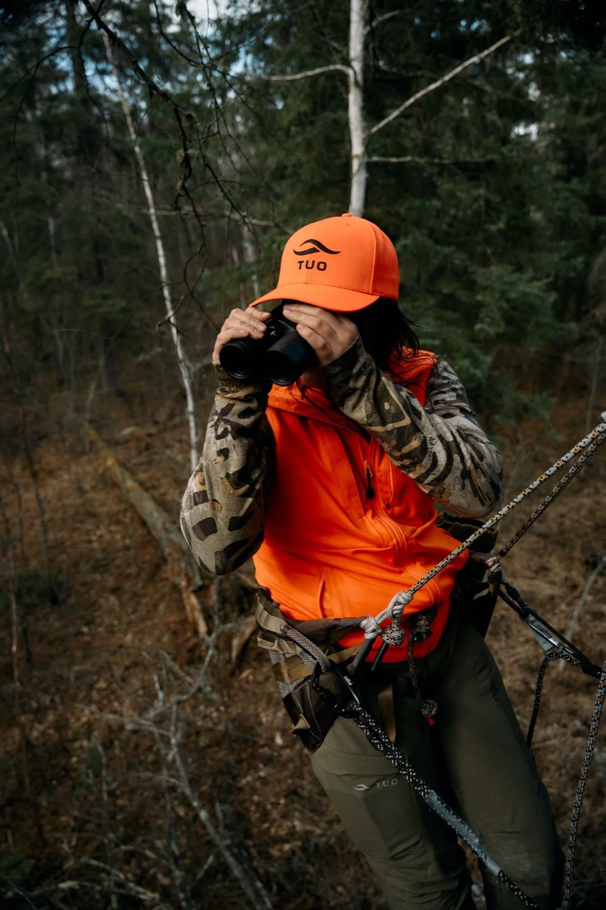 Hunter in an orange cap glassing with binoculars in the spruce