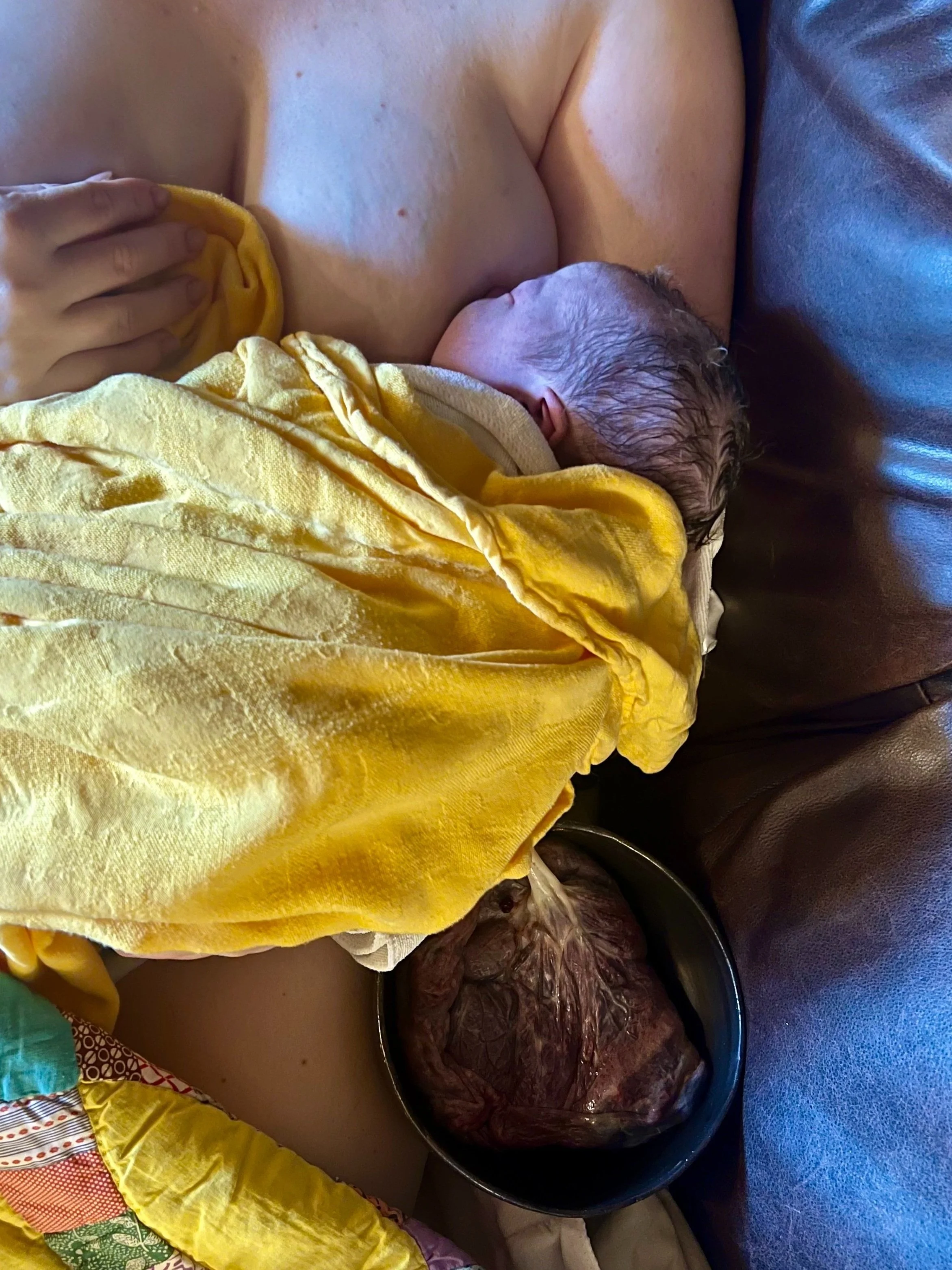 Newborn baby breastfeeding from mother lying on a couch with a yellow blanket.
