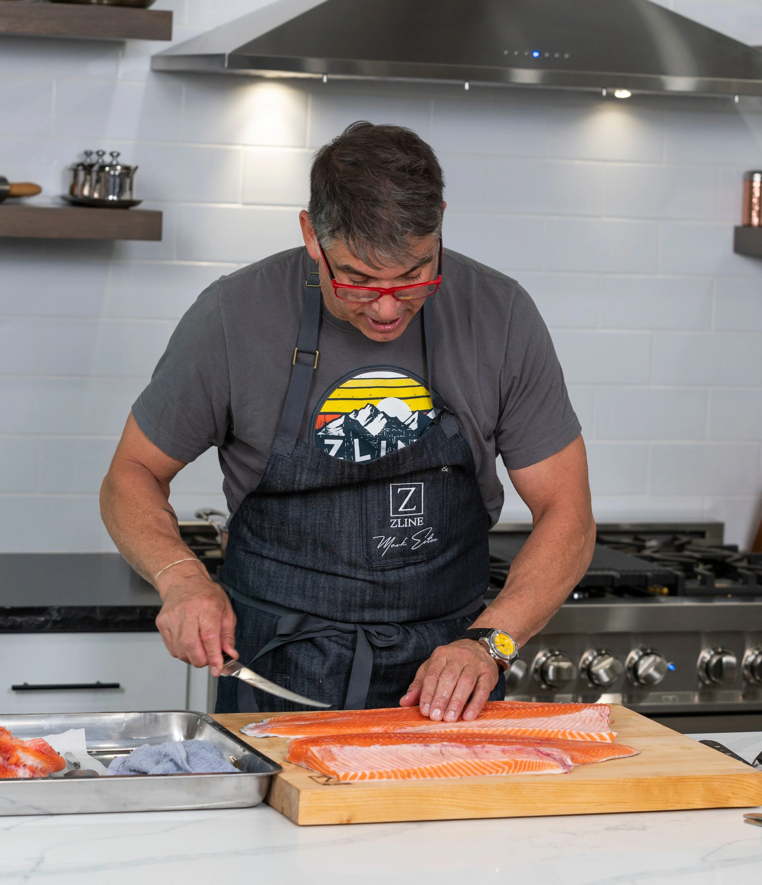 Person preparing raw salmon fillet on a wooden cutting board in a kitchen.