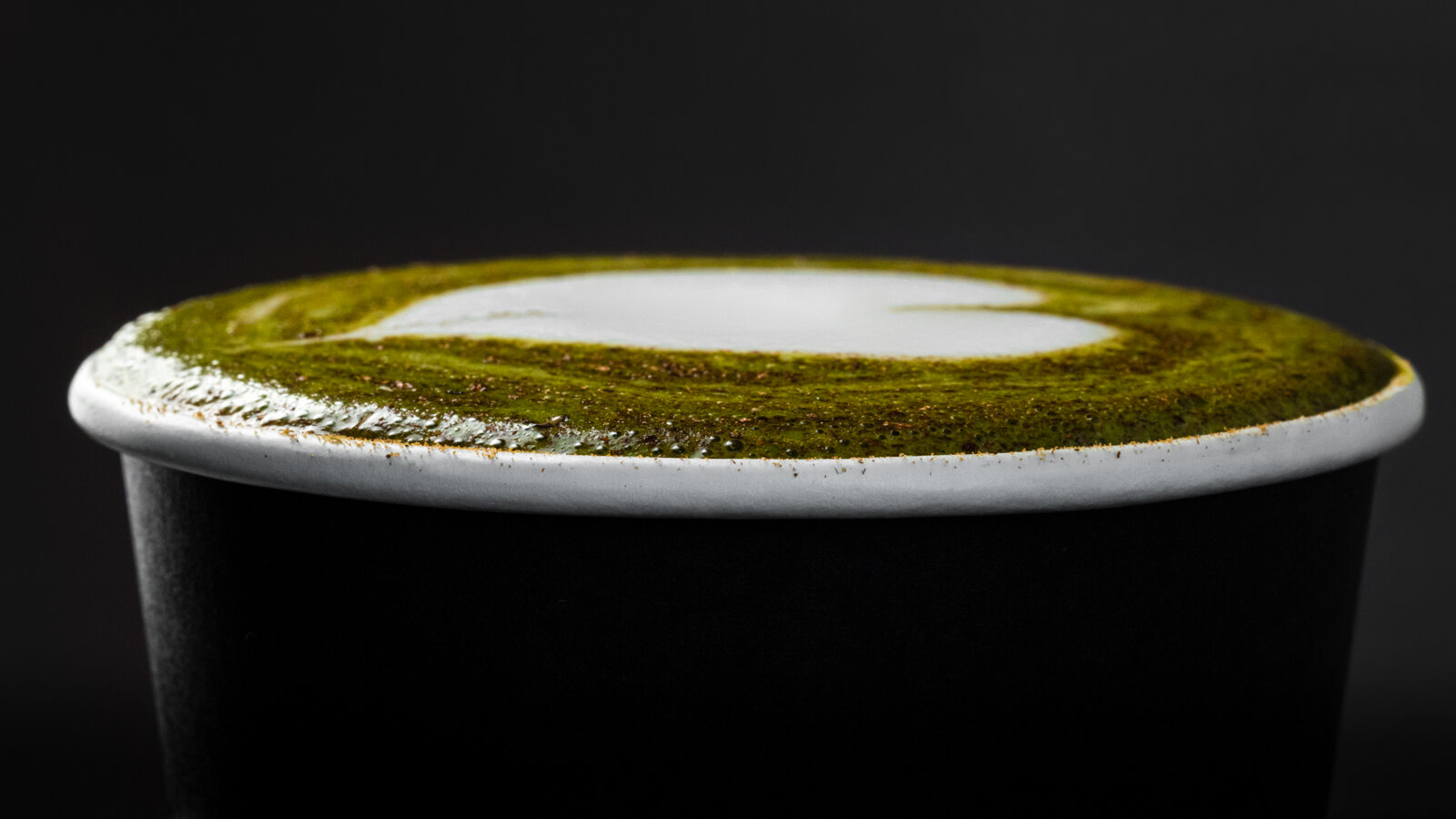 Close-up of a matcha latte in a black cup with heart-shaped foam.