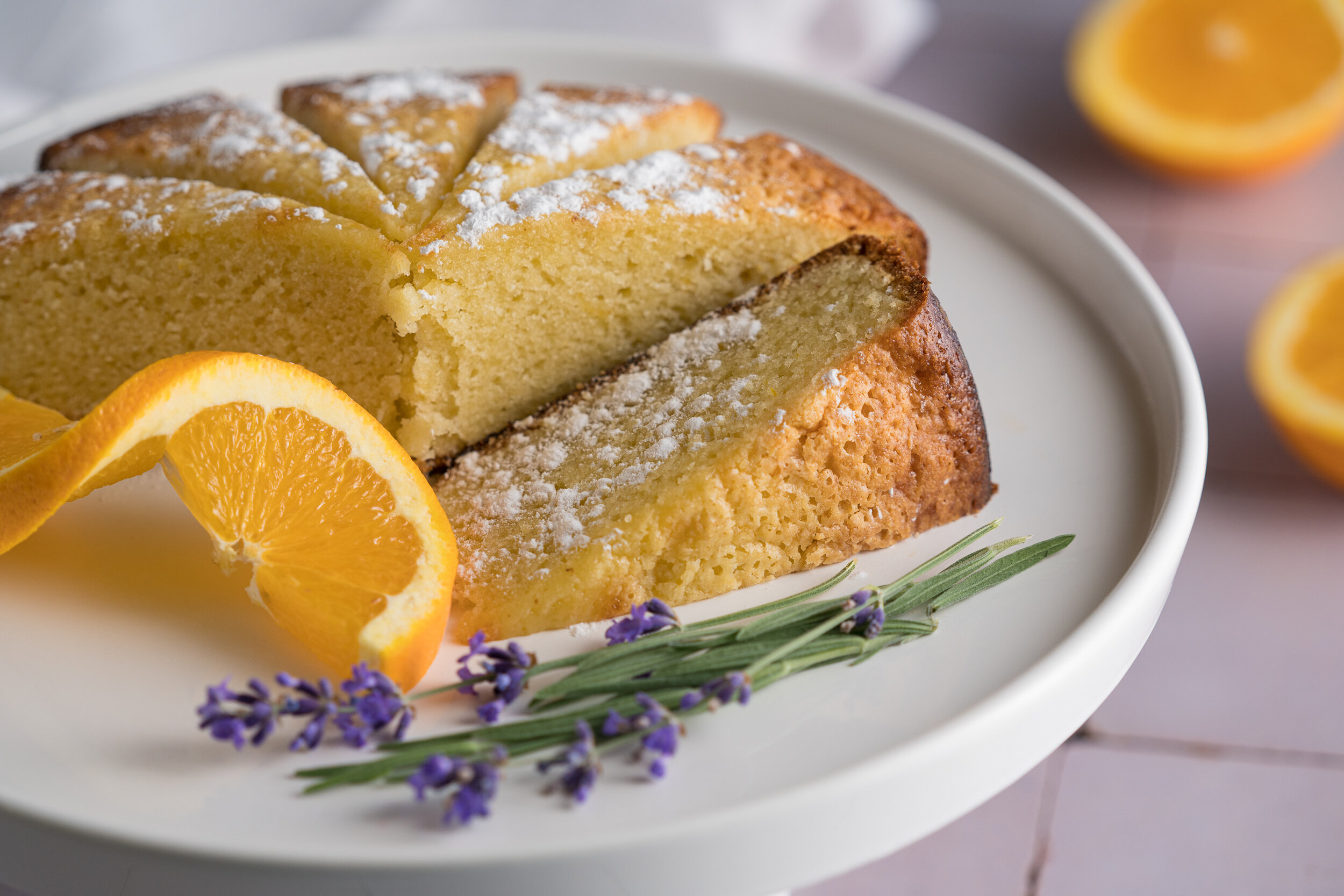 Lemon lavender cake sliced on a white cake stand, garnished with lavender sprigs and orange slices.