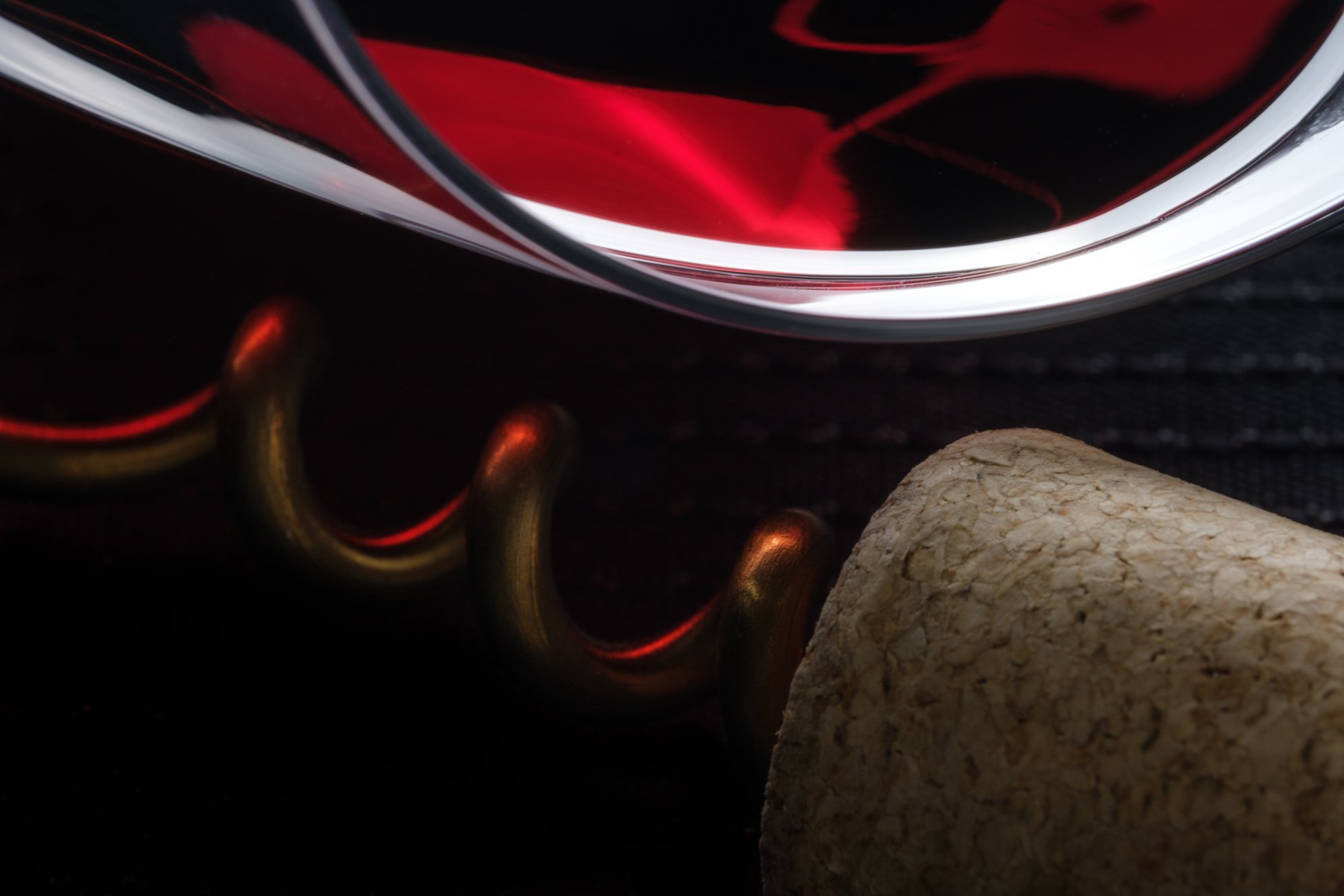 Close-up of a wine glass with red wine, a corkscrew, and a cork.