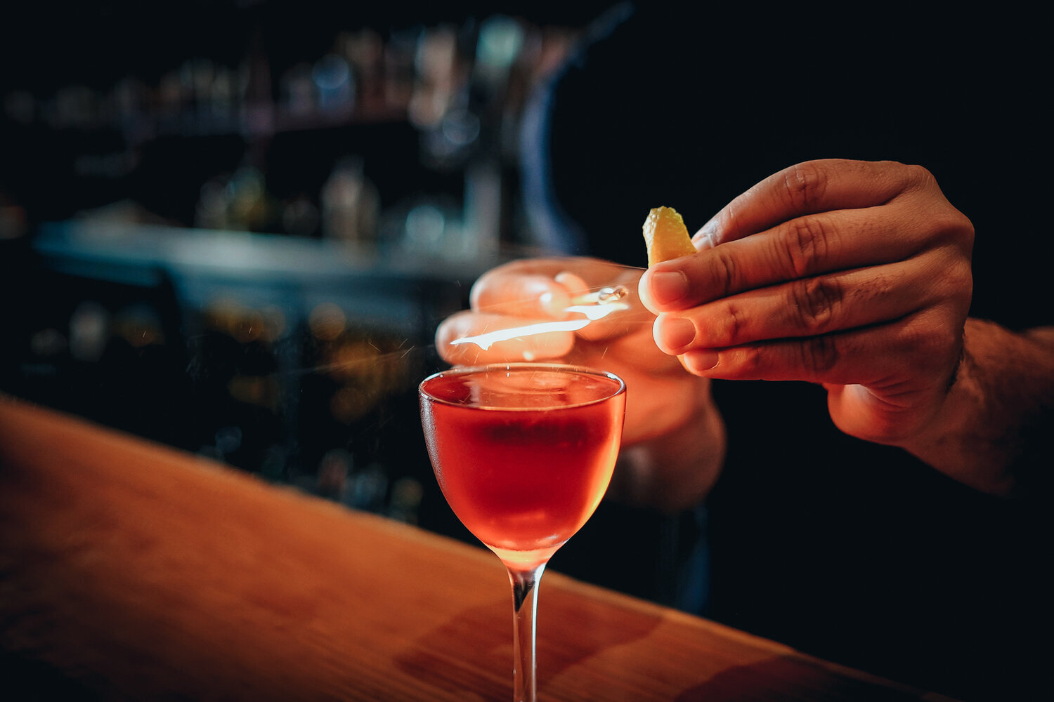 Bartender preparing cocktail with orange peel and flame.