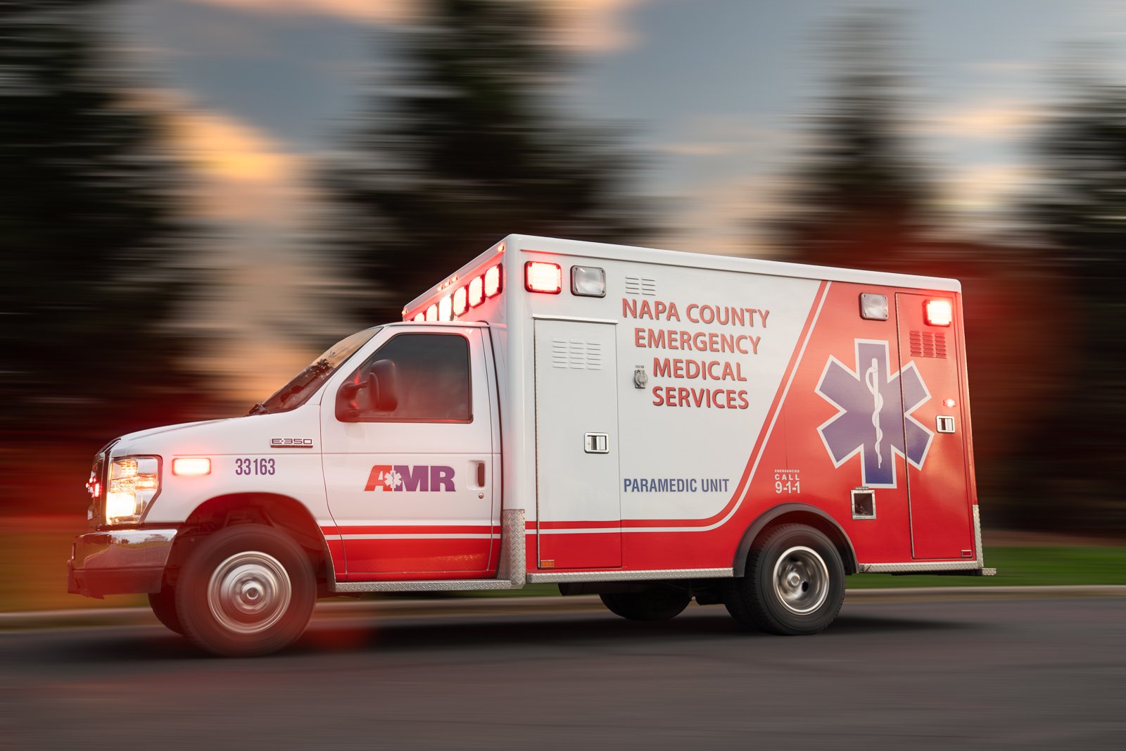 A speeding ambulance labeled "Napa County Emergency Medical Services" with flashing lights on a blurred background.