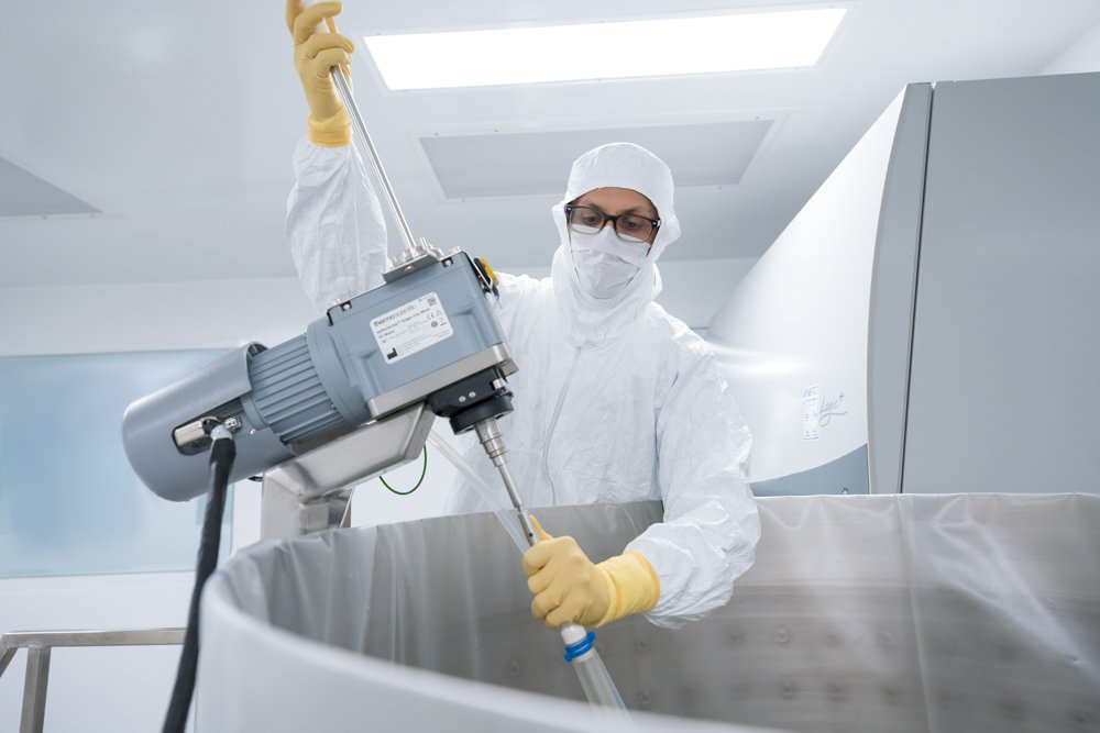Person in protective clothing using industrial equipment in a cleanroom environment.