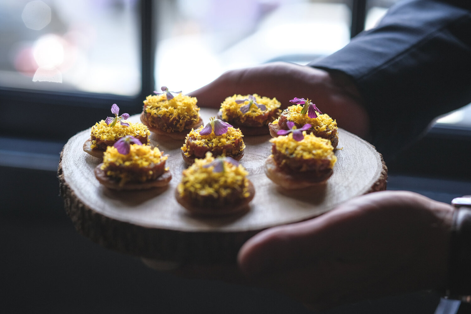 Small appetizers with yellow topping and purple garnish on a wooden platter.