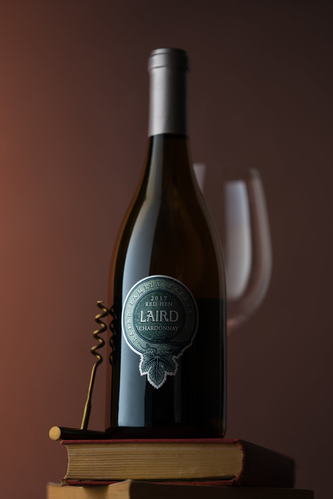 Bottle of Laird Family Estate Chardonnay wine on a stack of books with a corkscrew and wine glass in the background.