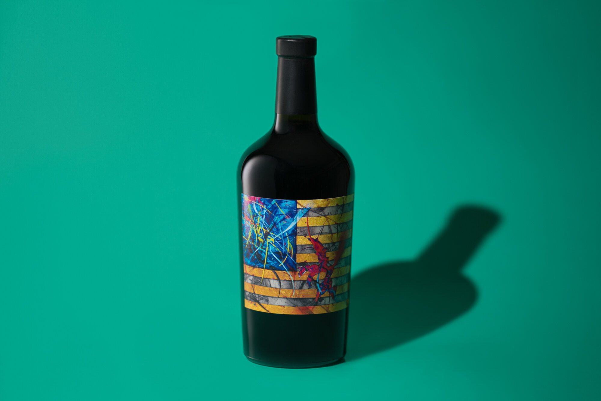 Dark wine bottle with colorful abstract label on green background.