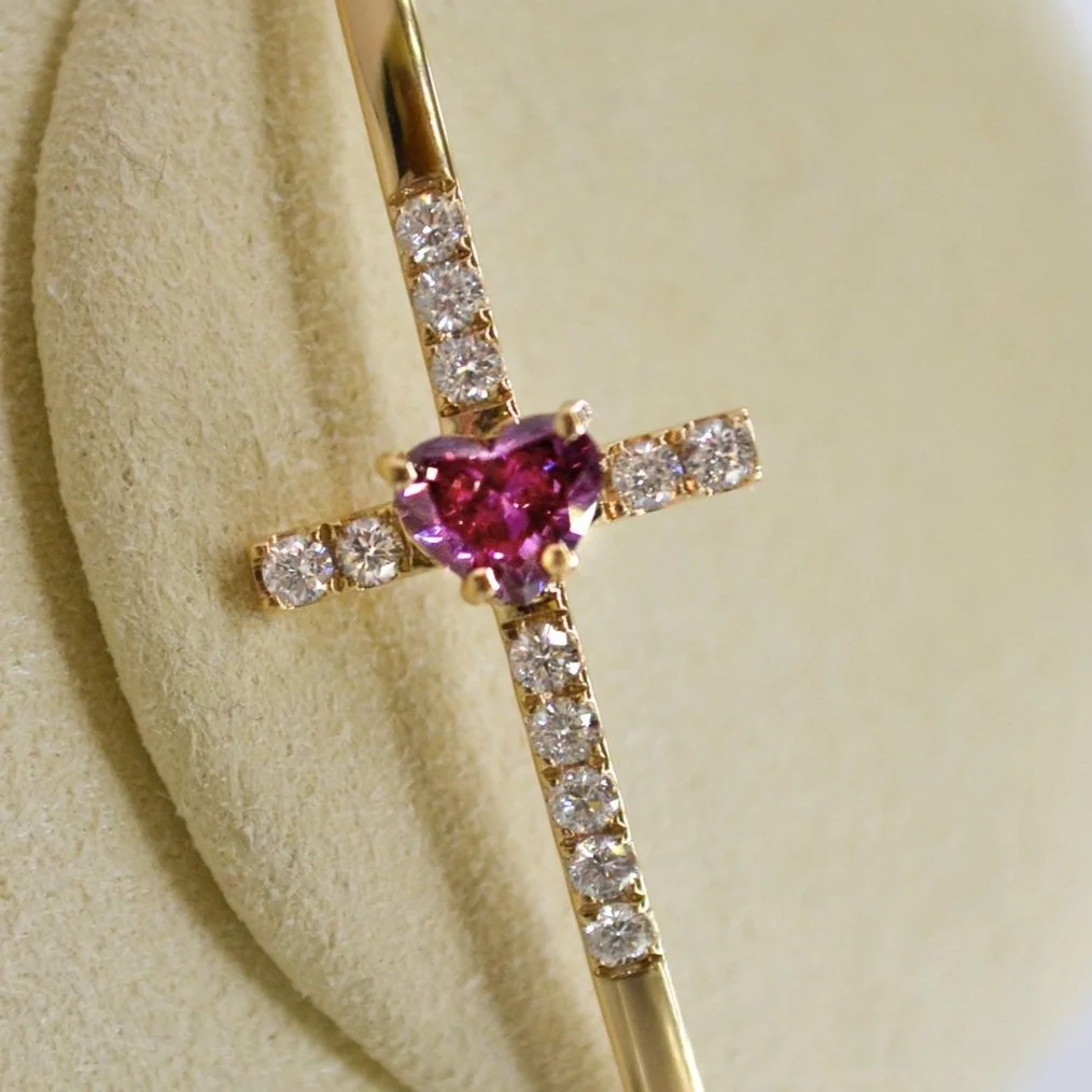 A refined gold bangle with a central pink heart diamond and accenting lots of small diamonds, representing everlasting love and remembrance.