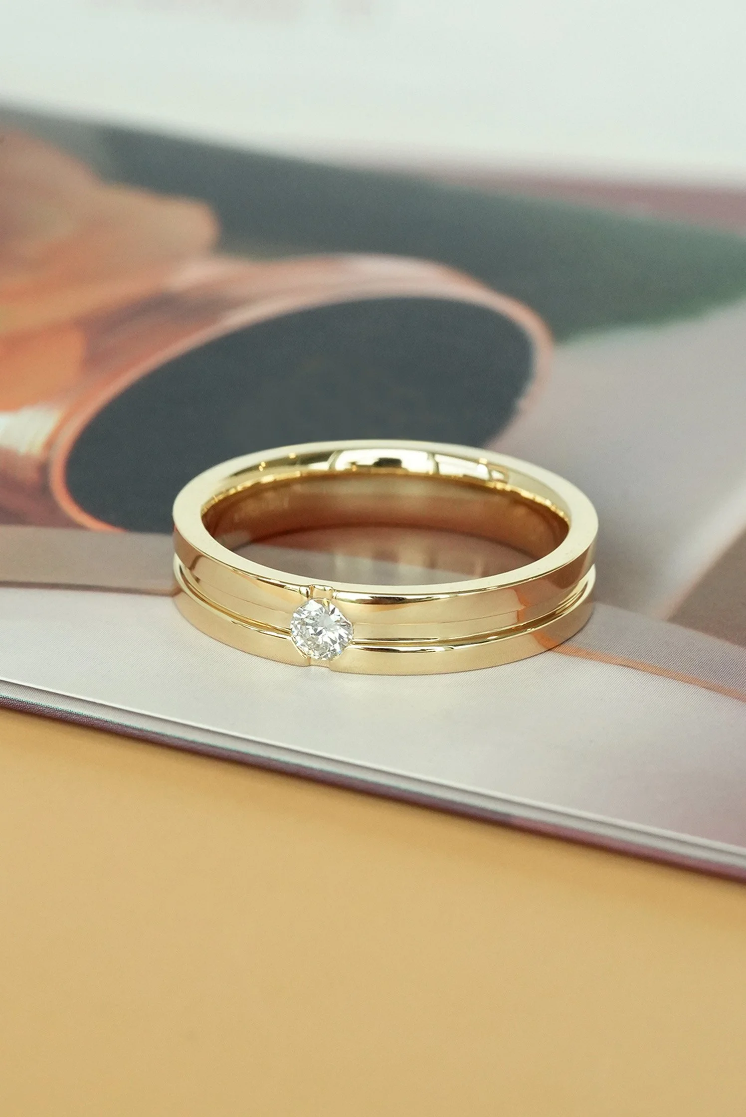 A polished 18k yellow gold ring with a sleek band, featuring a single sparkling diamond set in the center.