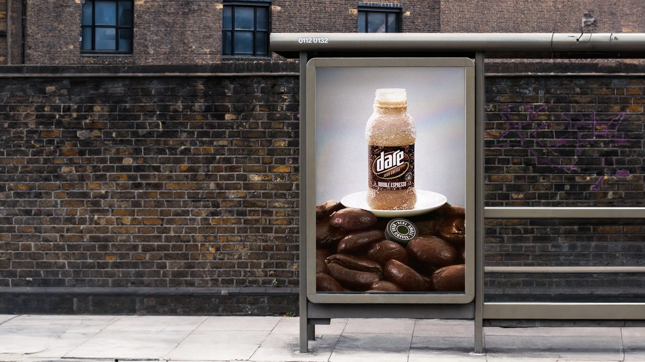 A bus stop advertisement featuring a bottle of dare ice coffee with a background of giant sized roasted coffee beans and stones, positioned against a brick wall.