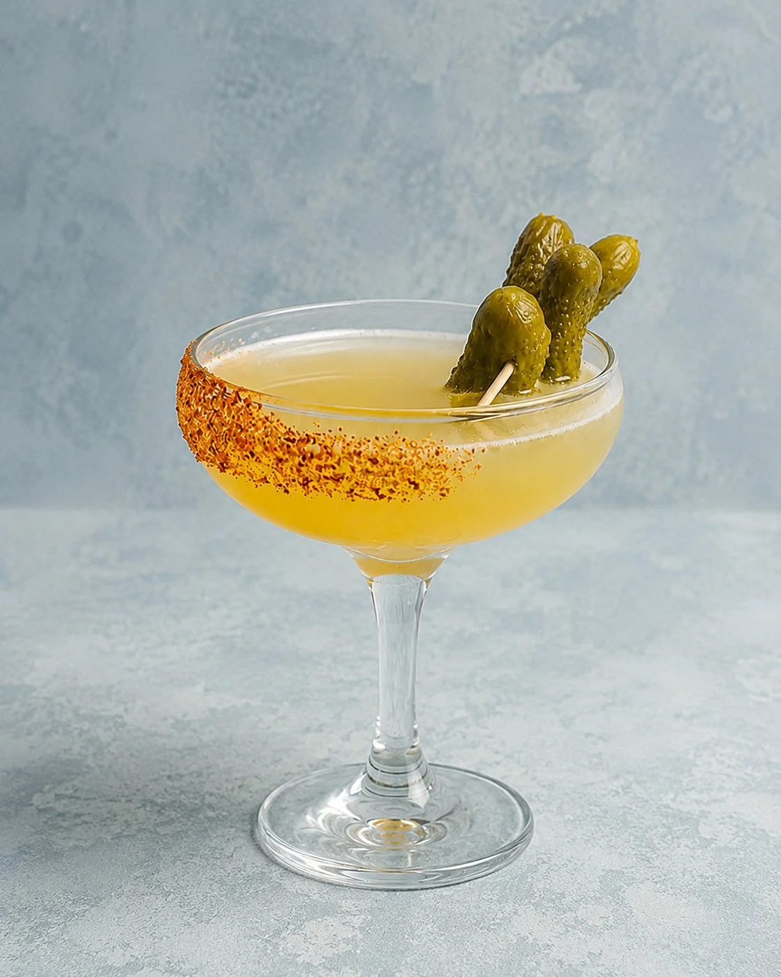 A Spicy Margarita cocktail with a tajin rim served in a coupe glass with a pickle garnish