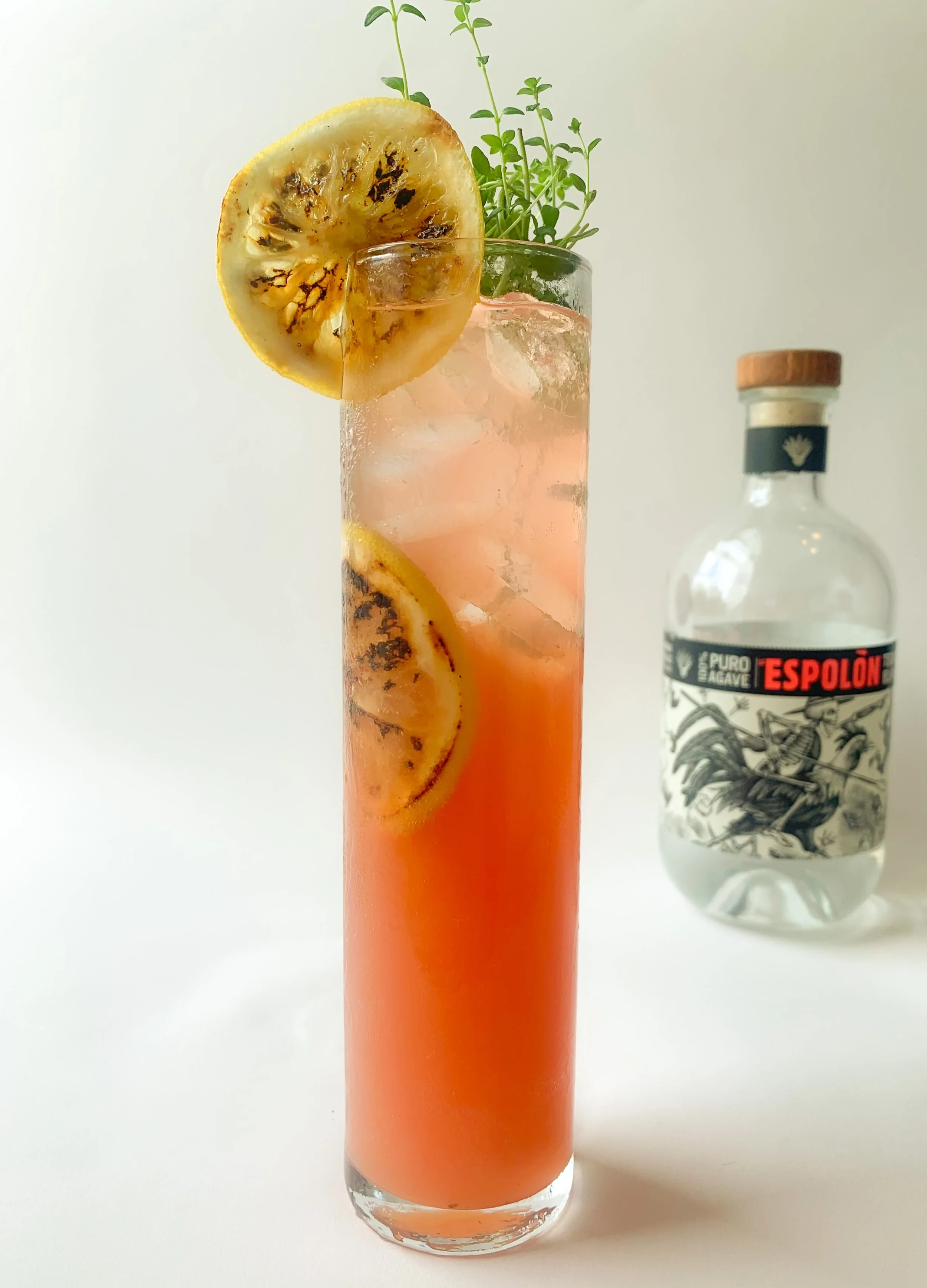 A paloma cocktail served in a highball glass garnished with a lemon wheel and fresh thyme