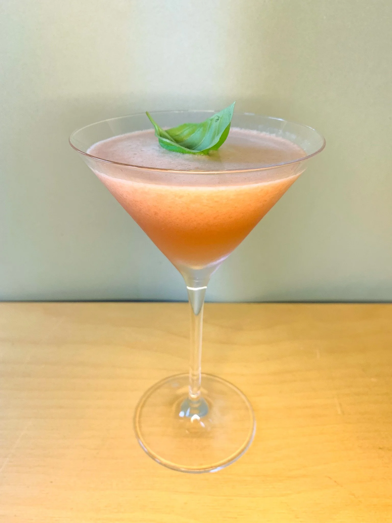 A watermelon martini served in a coupe glass garnished with a fresh basil leaf