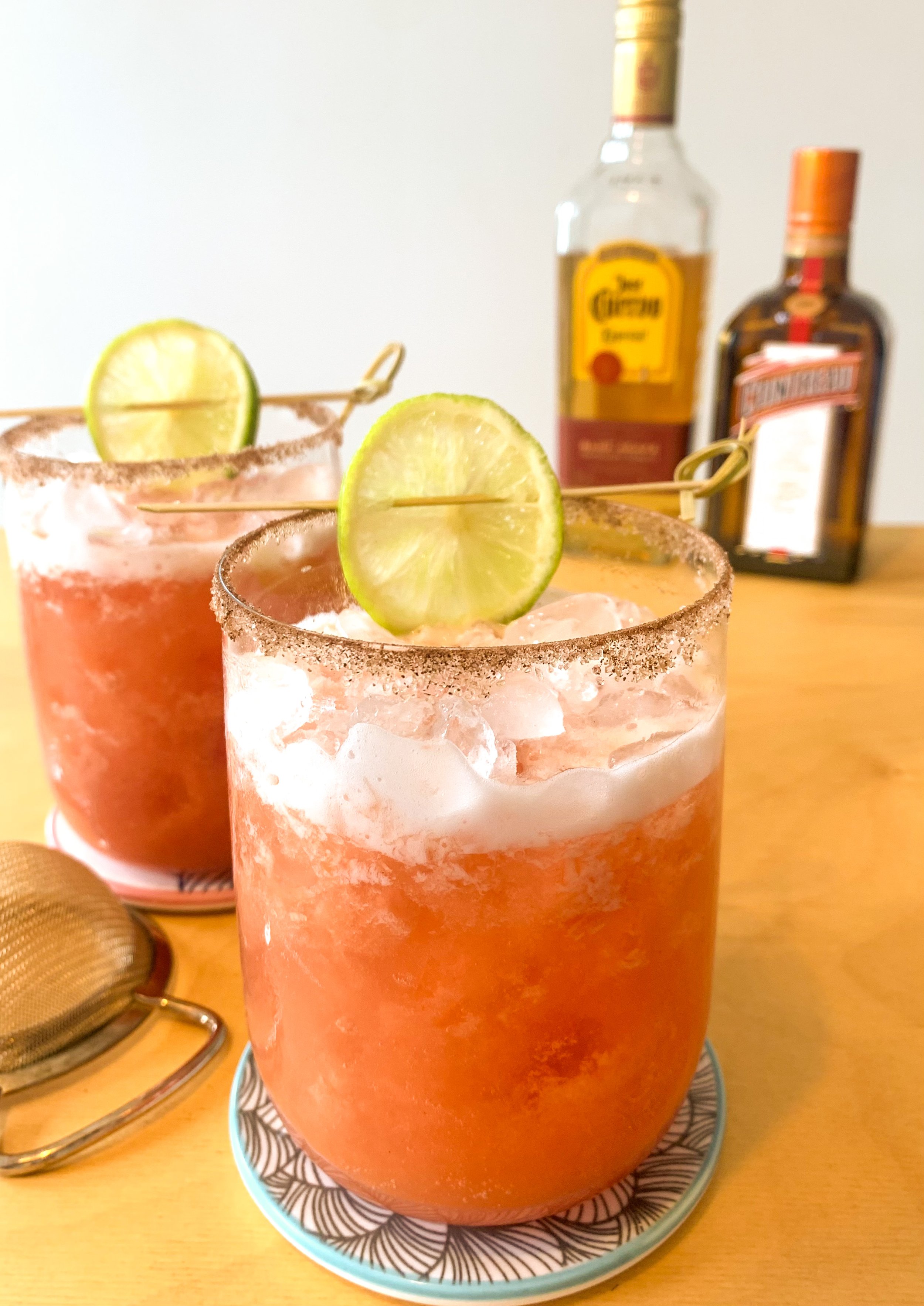 A Spicy Margarita cocktail served in a large rocks glass with a cinnamon sugar rim and garnished with a skewered lime wheel and
