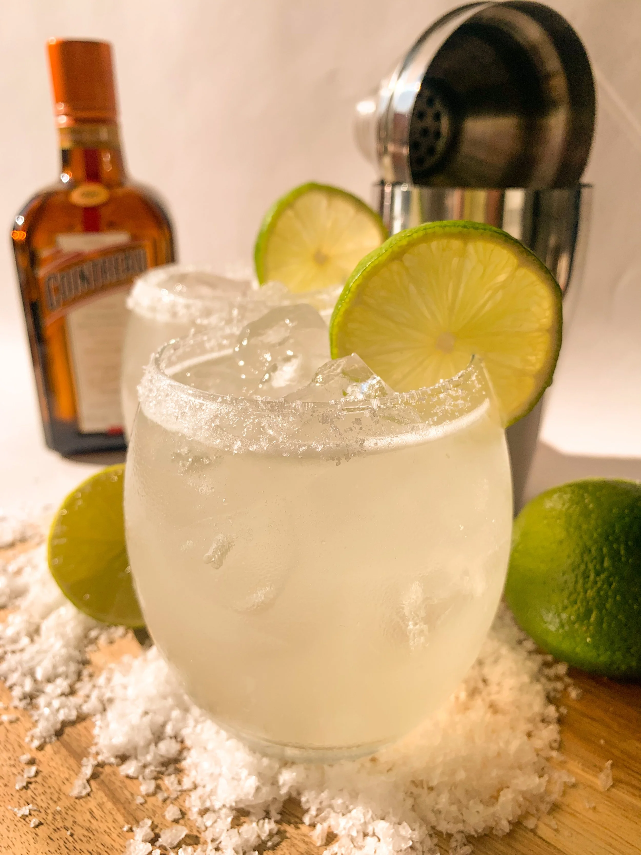 A margarita cocktail served over ice in a rocks glass with a salt rime and garnished with a lime wheel