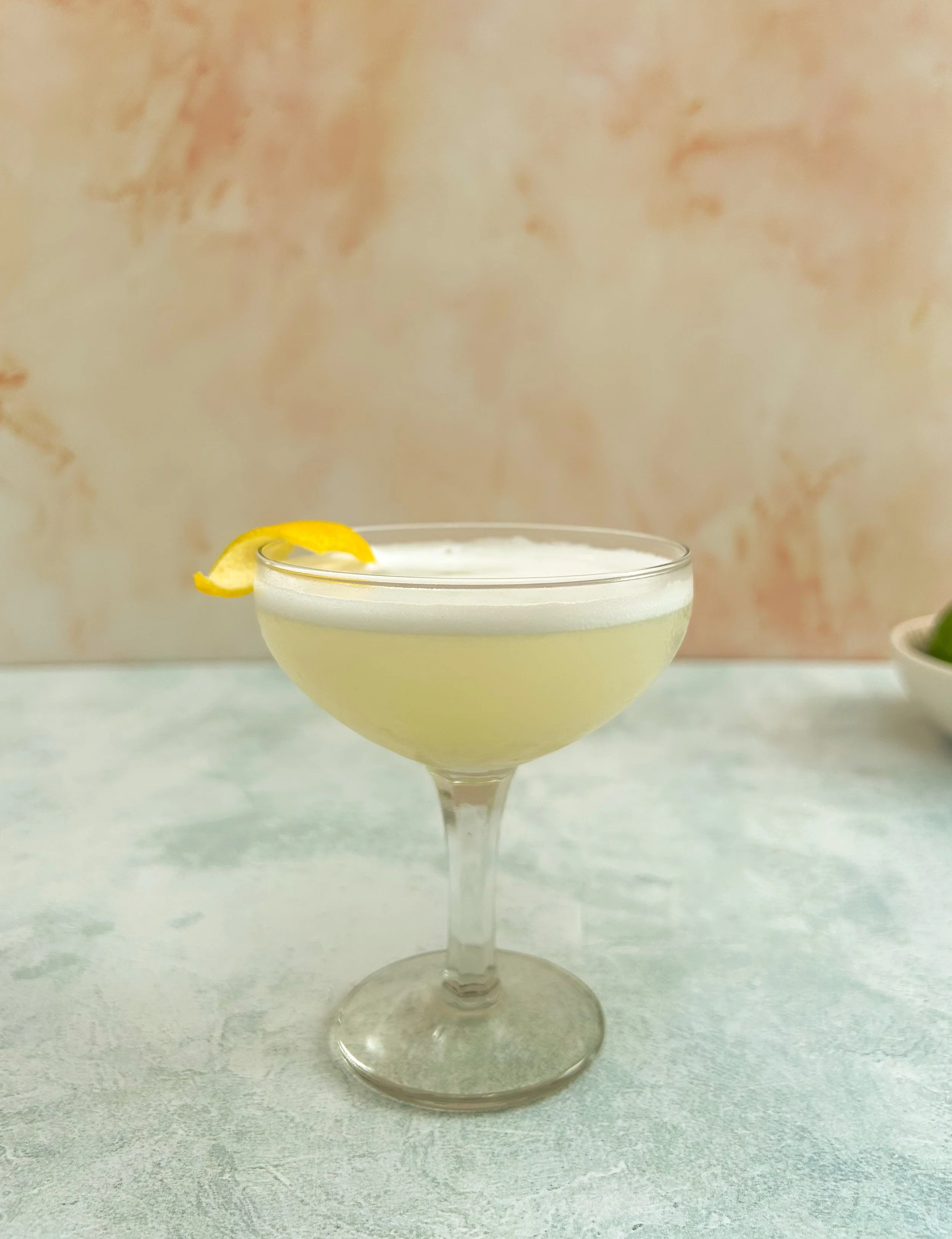 White Lady cocktail in a coupe glass garnished with a lemon rind