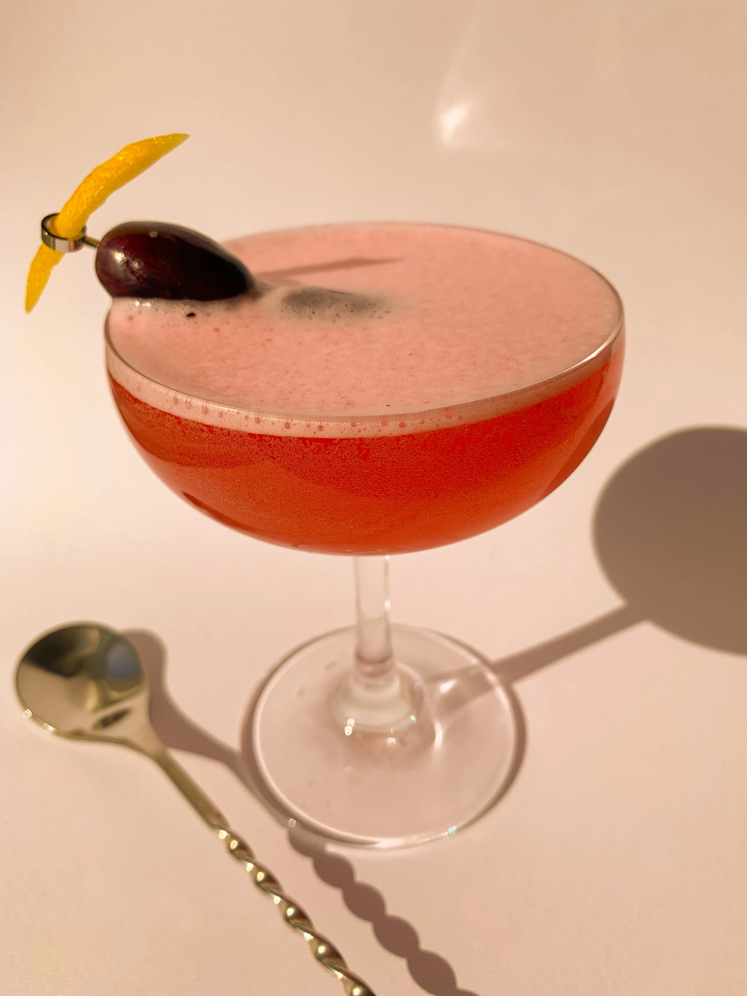 A Cosmopolitan cocktail served in a coupe glass garnished with a lemon twist