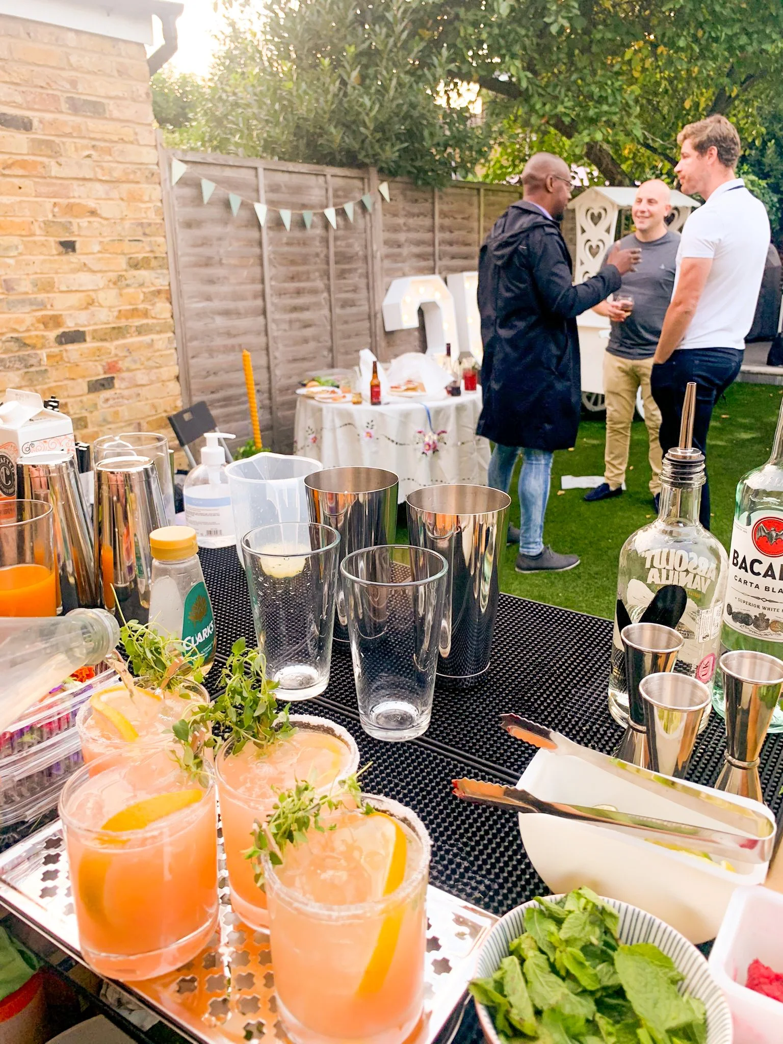 A paloma cocktail being served at a garden party served by a Brighton based mobile cocktail bar with three happy guests talking in the background