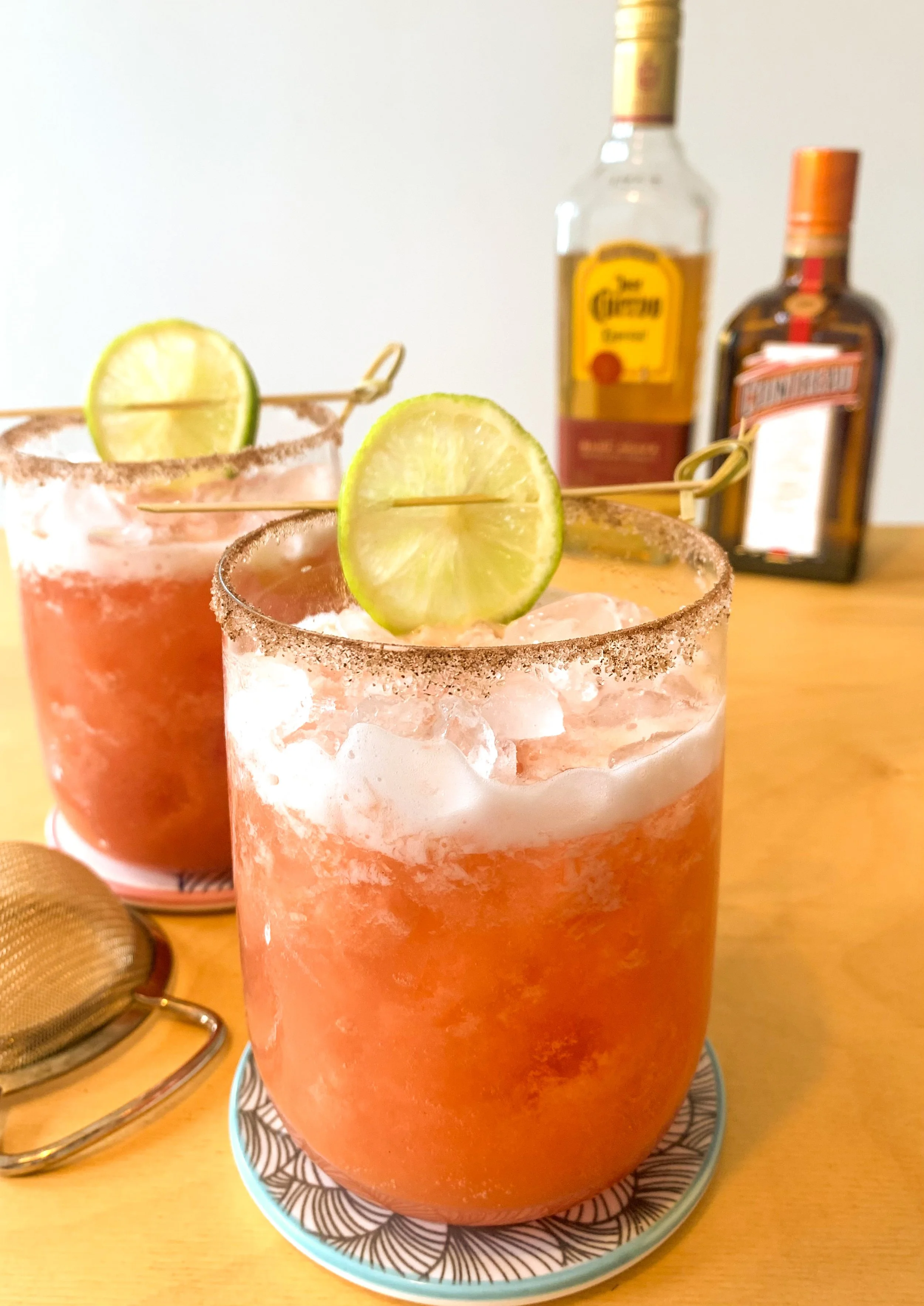 A spicy guava margarita cocktail served over ice in a large rocks glass with a cinnamon sugar rim and a skewered lime wheel garnish