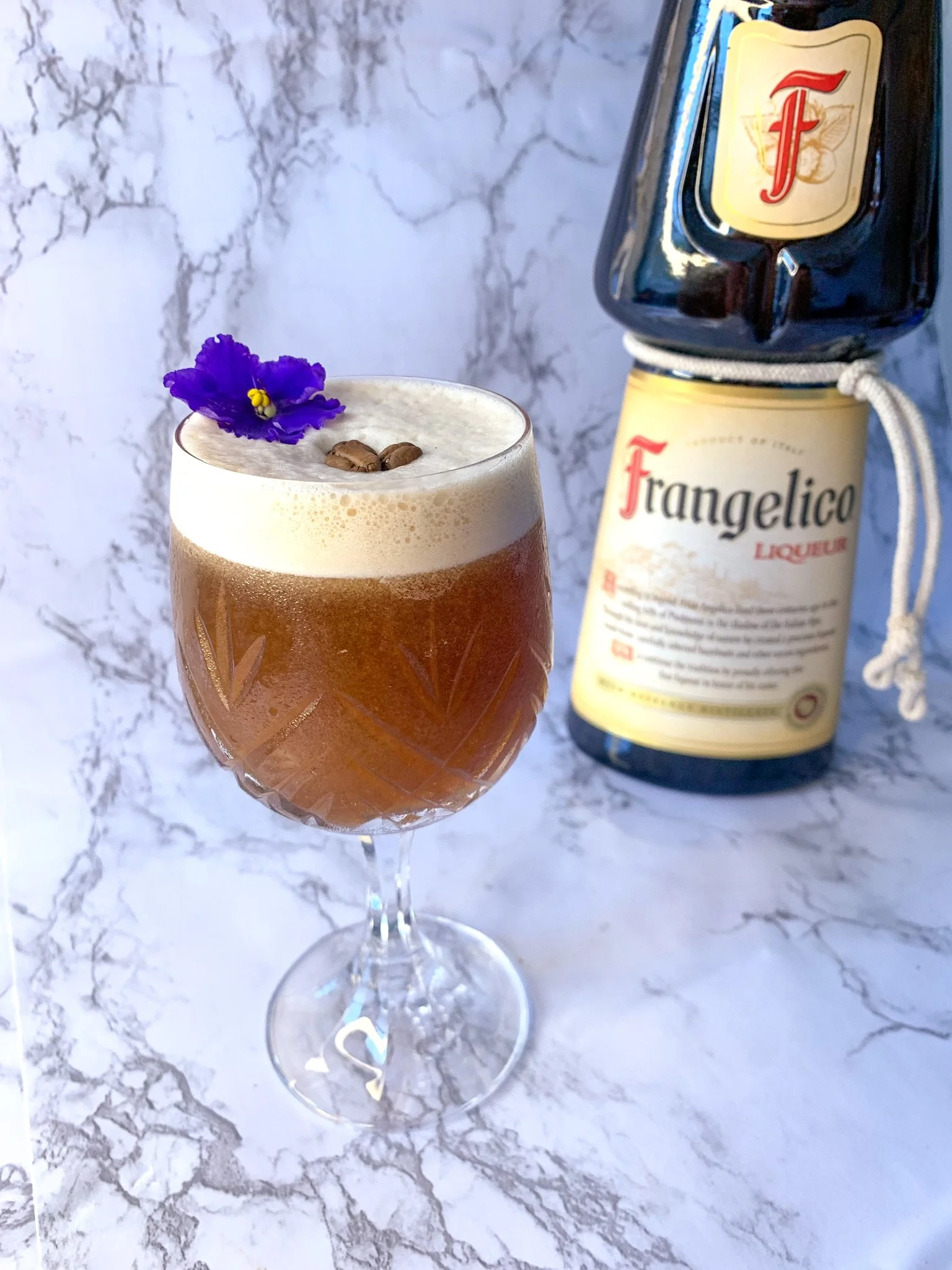 A mocha nut martini cocktail served in a cocktail glass garnished with coffee beans and a purple edible flower