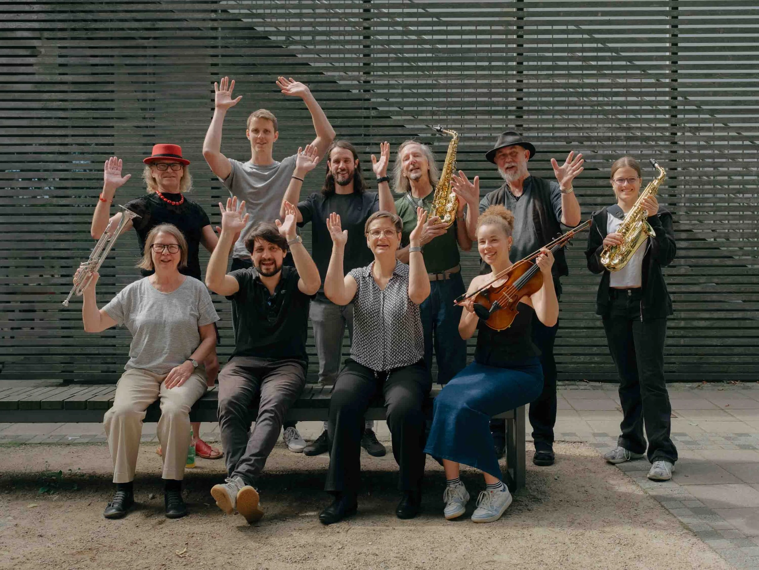 Teilnehmende des Jazzworkshop Lübeck auf einer Bank, die lachen und die Hände hochreißen