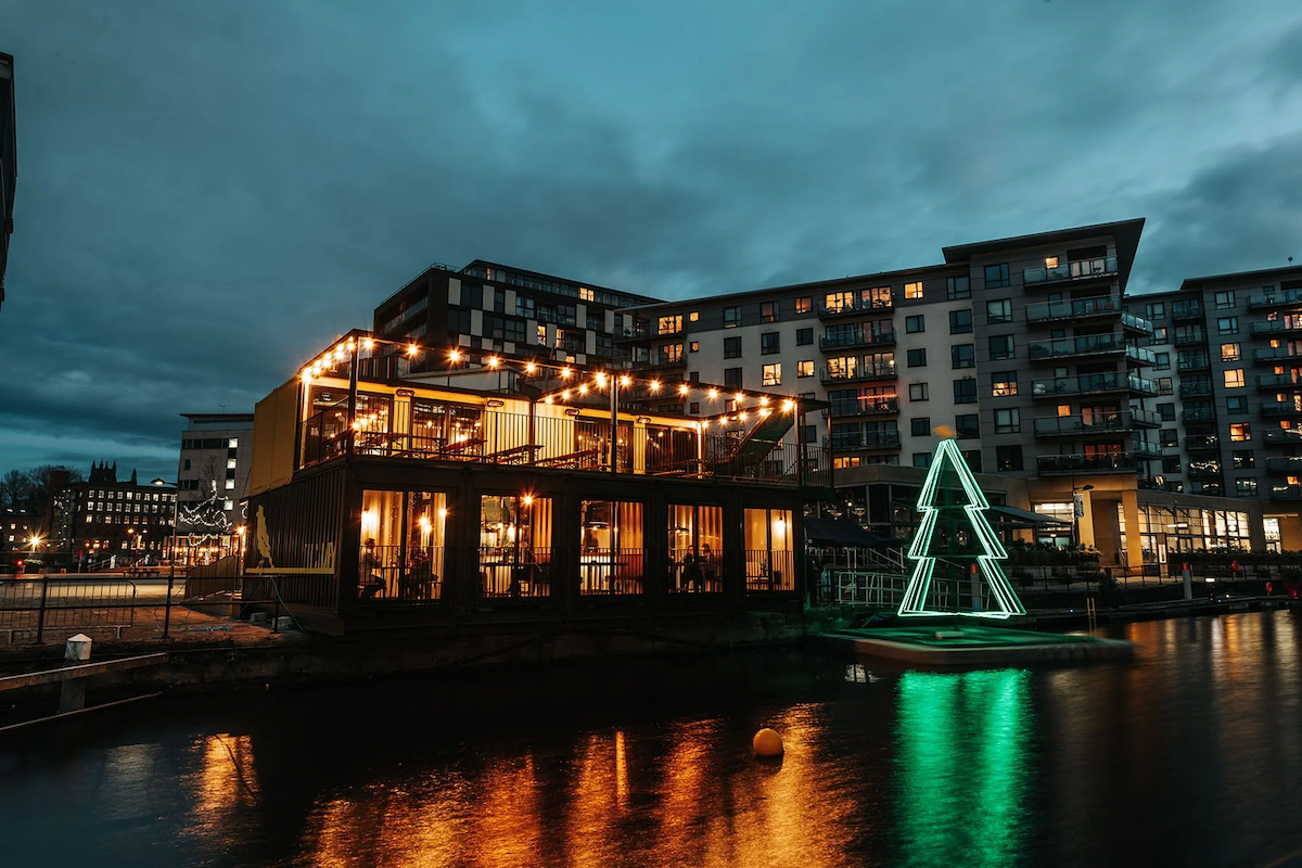 Nighttime view of a building by a waterway decorated with Christmas lights and a neon Christmas tree