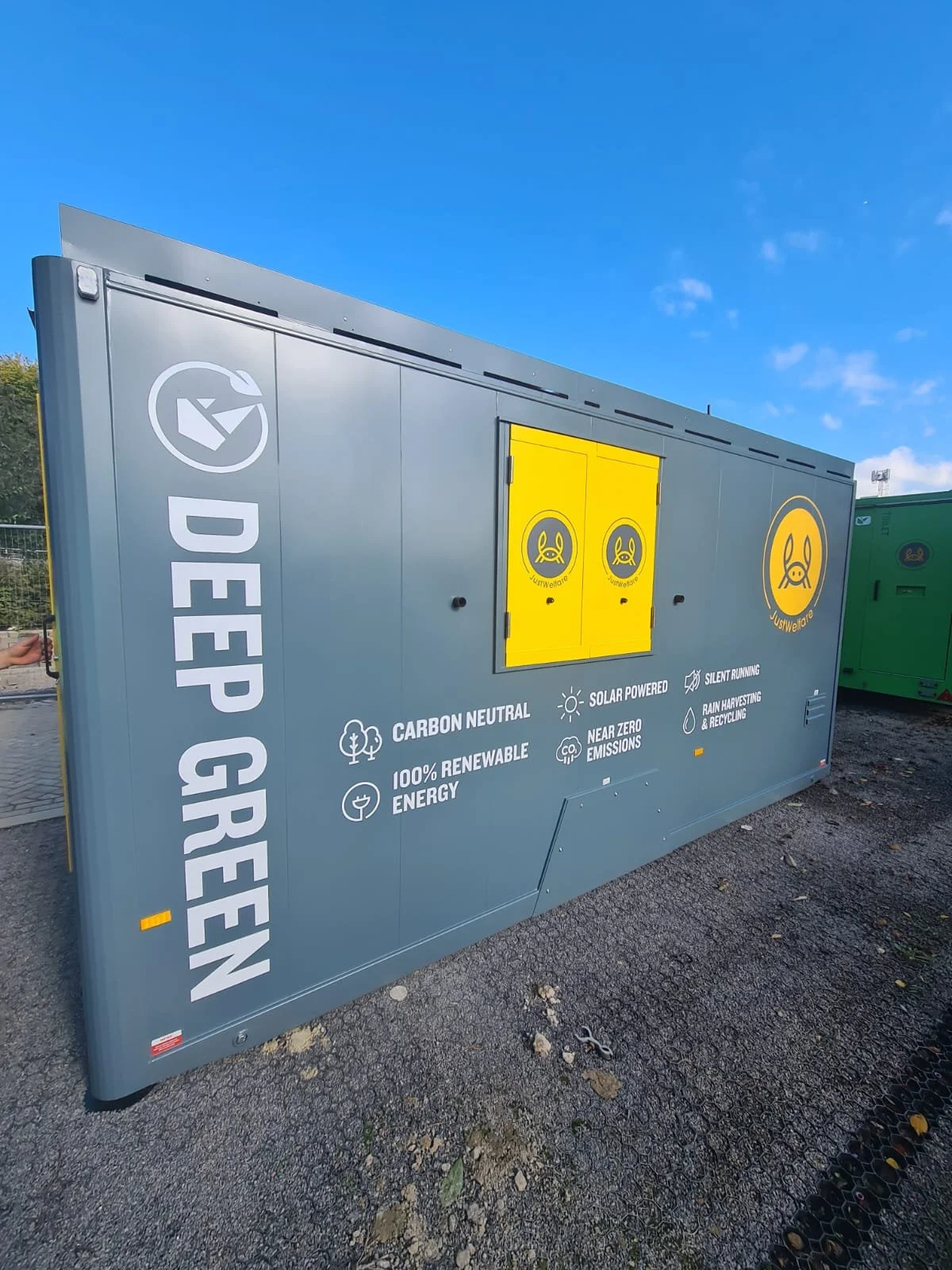 A gray container with yellow compartments and white text promoting eco-friendly energy solutions, including carbon neutrality, renewable energy, solar power, and rain harvesting, with the text 'DEEP GREEN' on the side.