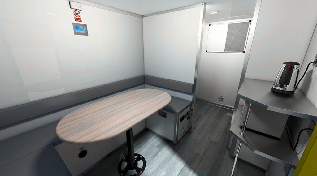 An empty hospital or medical isolation room with a small round table, a chair, a metal partition, and a small countertop with an electric kettle.