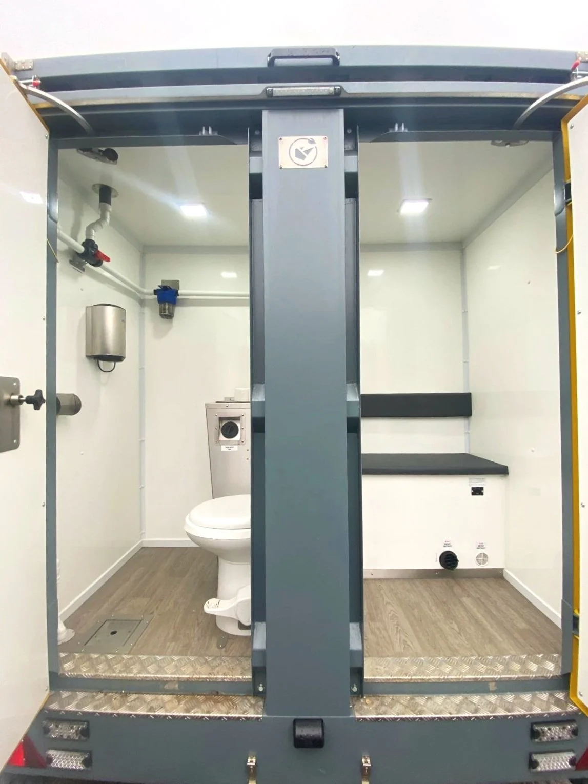 Inside a mobile bathroom unit with a toilet, sink, and black benches.