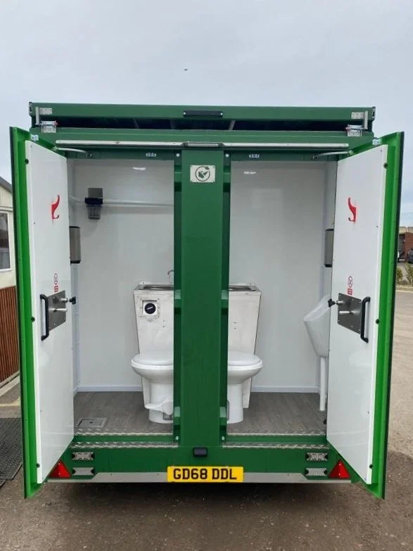 Mobile outdoor toilet with two separate stalls, each with a toilet, green exterior, and open doors.
