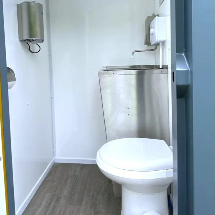 Small bathroom with a toilet, stainless steel sink with a small faucet, wall-mounted soap dispenser, and paper towel dispenser.