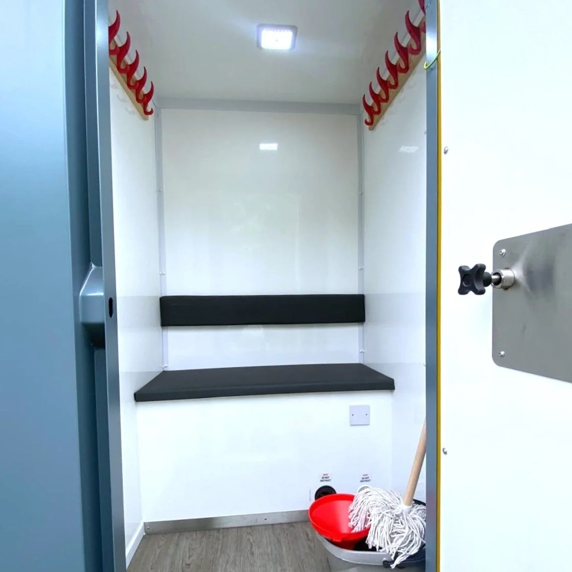 Empty cleaning room with black bench and hooks, mop, bucket, and cleaning supplies.