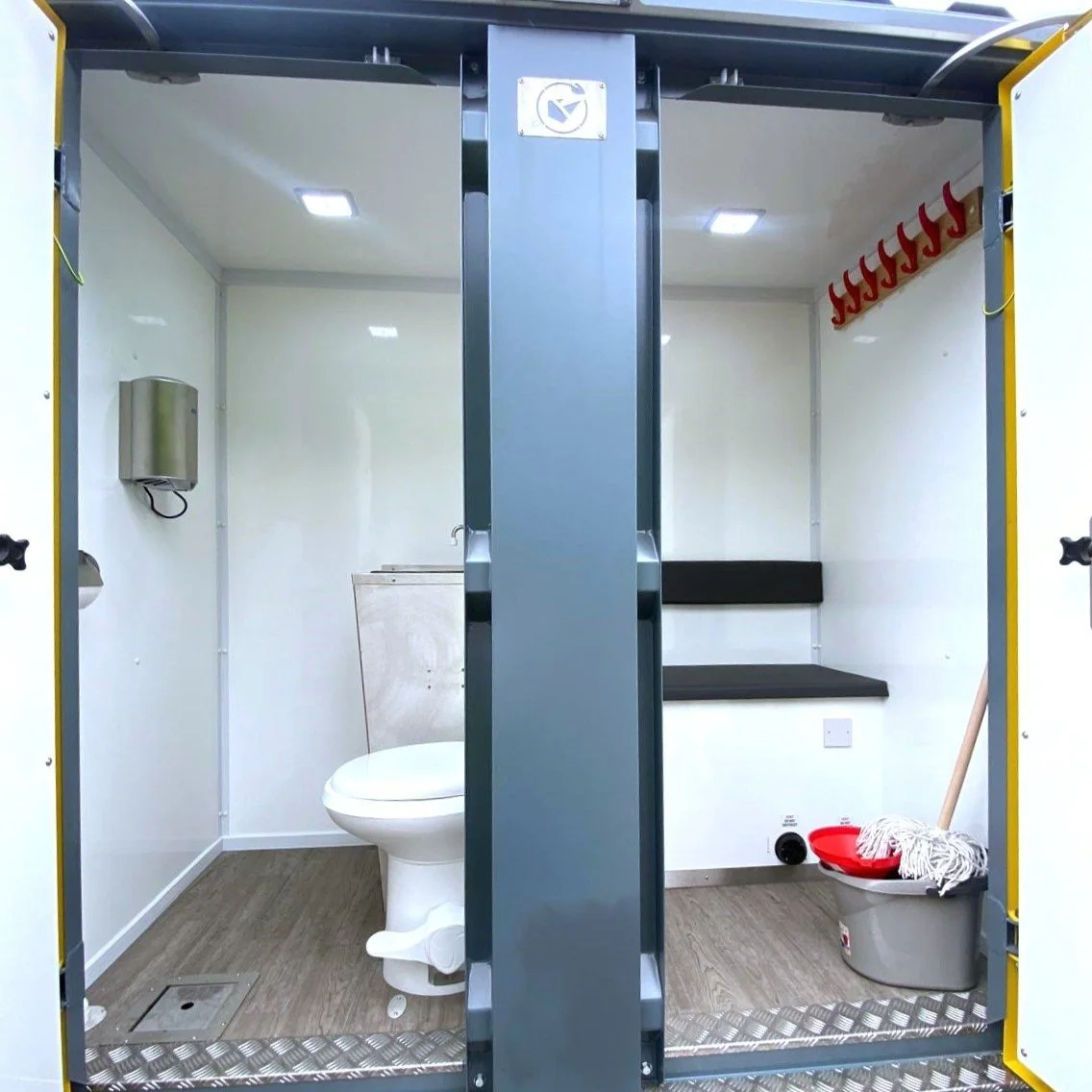 Empty portable cleaning or restroom facility with a toilet, mop, bucket, and hanging hooks.