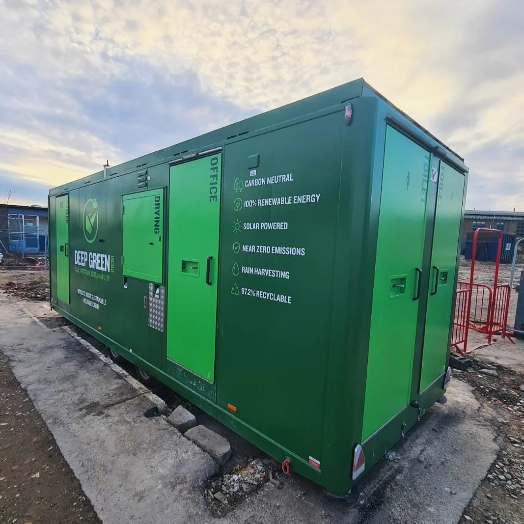 Green portable unit with eco-friendly features listed, including carbon neutrality, renewable energy, solar power, near zero emissions, rain harvesting, and high recyclability, set outdoors on construction site or industrial area.