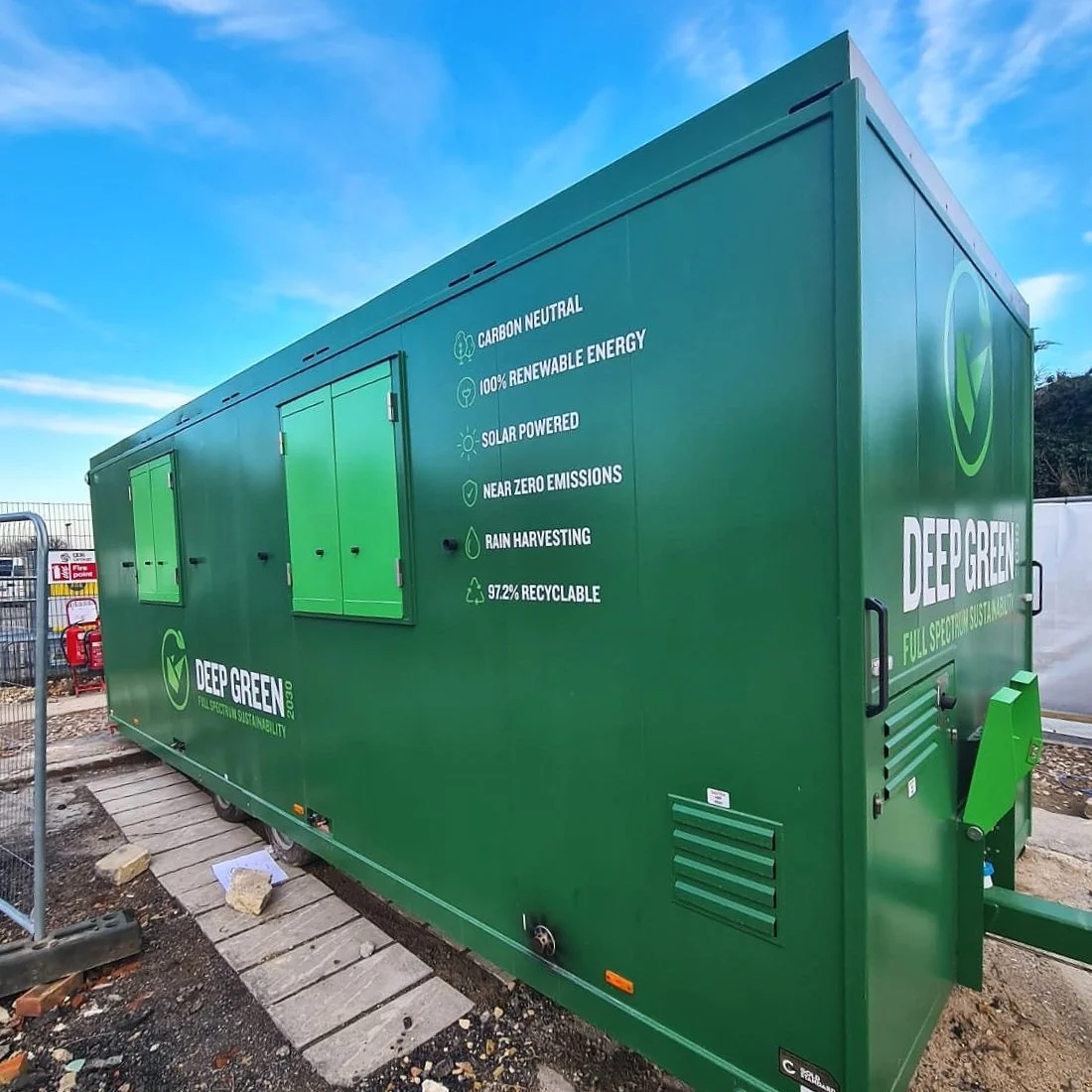 Green mobile unit with sustainability features and logos, displaying eco-friendly attributes including carbon neutrality, renewable energy, solar power, zero emissions, rain harvesting, and recyclability.