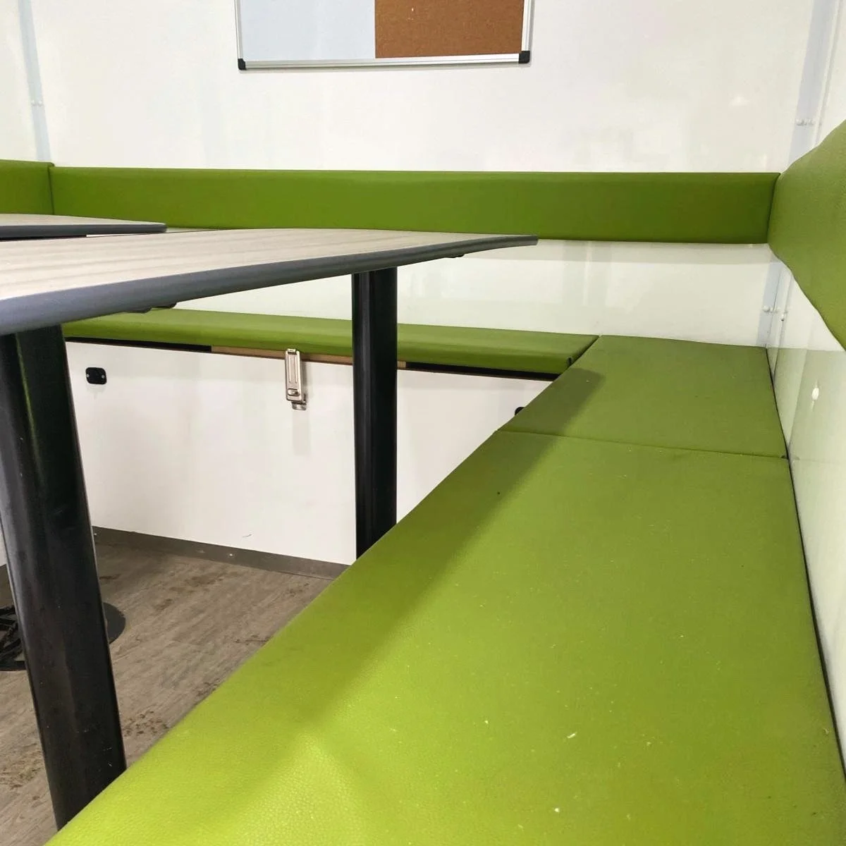 Café style corner booth with green cushioned seating and a gray table, inside a modern room.