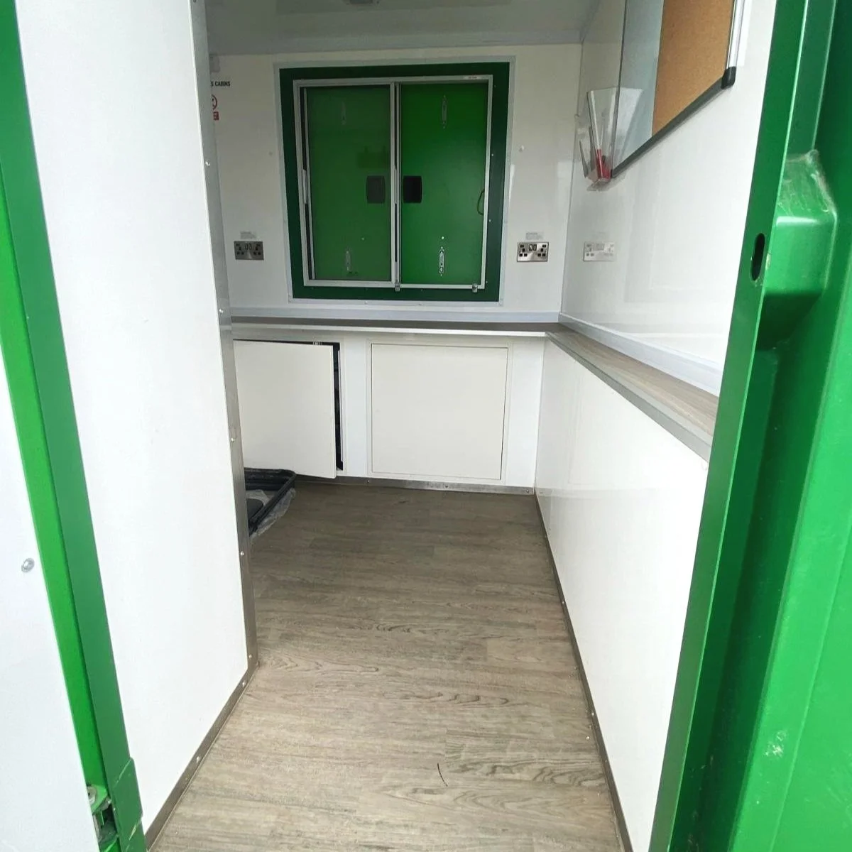 Small green and white electrical or control room with a window, cabinets, and outlets.