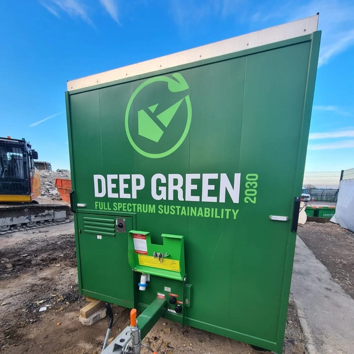 A large green unit with the label "Deep Green 2030" and eco-friendly messaging, situated outdoors at a construction site with equipment and dirt around.